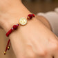 Mano de modelo usando una pulsera tejida en hilo color rojo con dije de San Benito en oro amarillo de 18 quilates con cristales de color blanco de Joyería Caracas. 