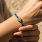 Mano de modelo usando una pulsera tejida en hilo color celeste con dije del Arcángel San Gabriel en oro amarillo de 18 quilates con bisutería de calidad de Joyería Caracas.