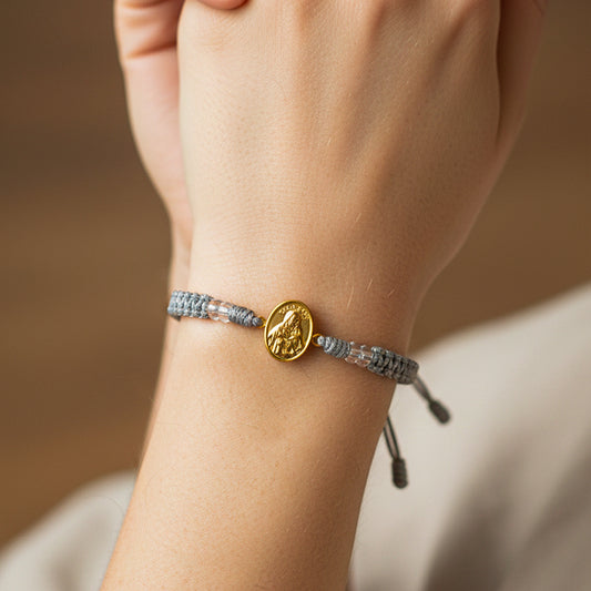 Mano de modelo usando una pulsera tejida en hilo color gris con accesorios y herraje de San José de Joyería Caracas. 