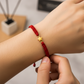 Mano de modelo usando una pulsera tejida en hilo color rojo con dije en forma de estrella en oro amarillo de 18 quilates de Joyería Caracas. 
