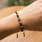 Mano de modelo usando una pulsera tejida en hilo de color negro, con piedra amatista y esferas lisas en oro amarillo de 18 quilates de Joyería Caracas. 