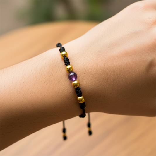 Mano de modelo usando una pulsera tejida en hilo de color negro, con piedra amatista y esferas lisas en oro amarillo de 18 quilates de Joyería Caracas. 