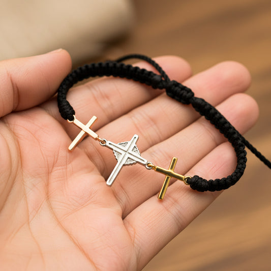 Mano de modelo usando una pulsera tejida en hilo color negro con dije de tres cruces en tres oros de 18 quilates de Joyería Caracas. 