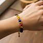 Mano de modelo usando una pulsera tejida en hilo color negro, con esferas lisas en oro amarillo de 18 quilates y bisutería de calidad de Joyería Caracas. 