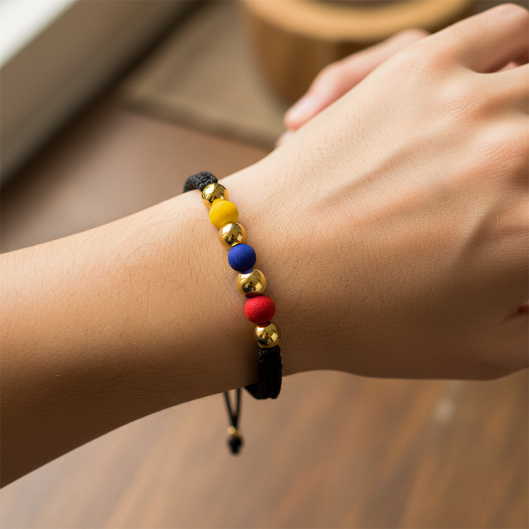 Mano de modelo usando una pulsera tejida en hilo color negro, con esferas lisas en oro amarillo de 18 quilates y bisutería de calidad de Joyería Caracas. 