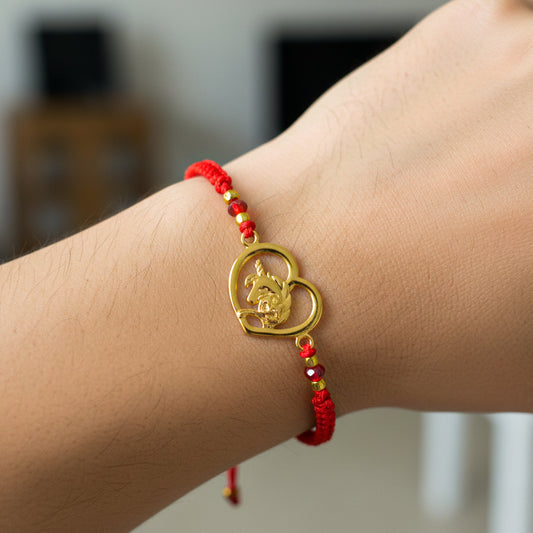 Mano de modelo usando una pulsera tejida en hilo color rojo con dije de unicornio en oro amarillo de 18 quilates con bisutería de calidad de Joyería Caracas. 