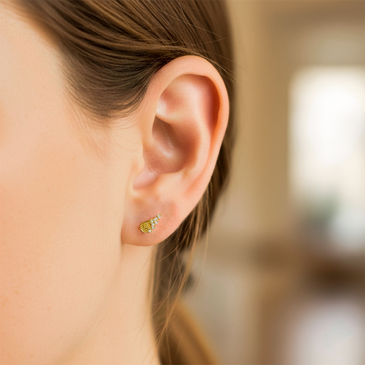 Oreja de modelo usando unos topitos en forma de ala de ángel en oro amarillo de 18 quilates con Diamantes en color blanco de Joyería Caracas.