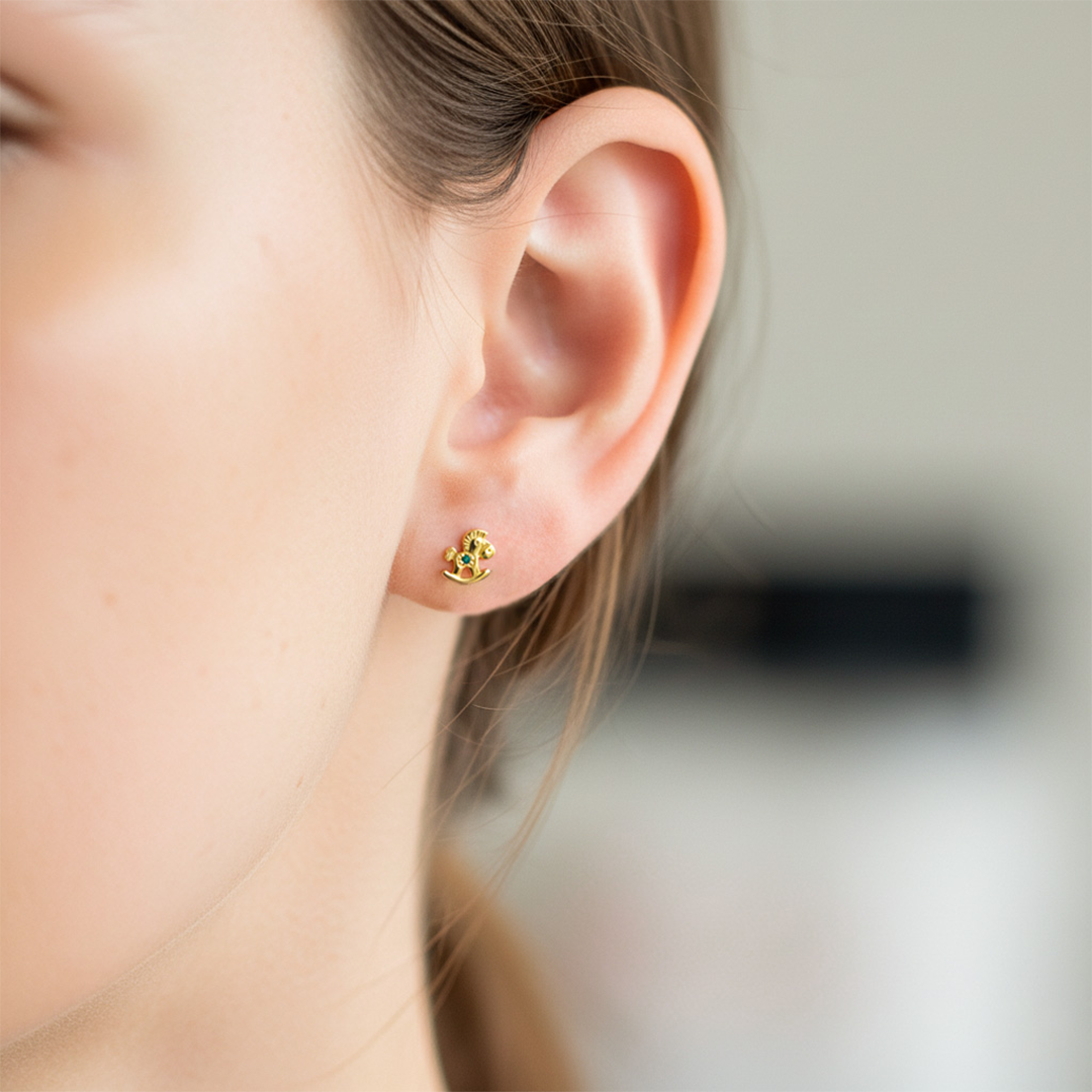 Oreja de modelo usando un topito en forma de caballo de palo en oro amarillo de 18 quilates con cristal de Joyería Caracas. 