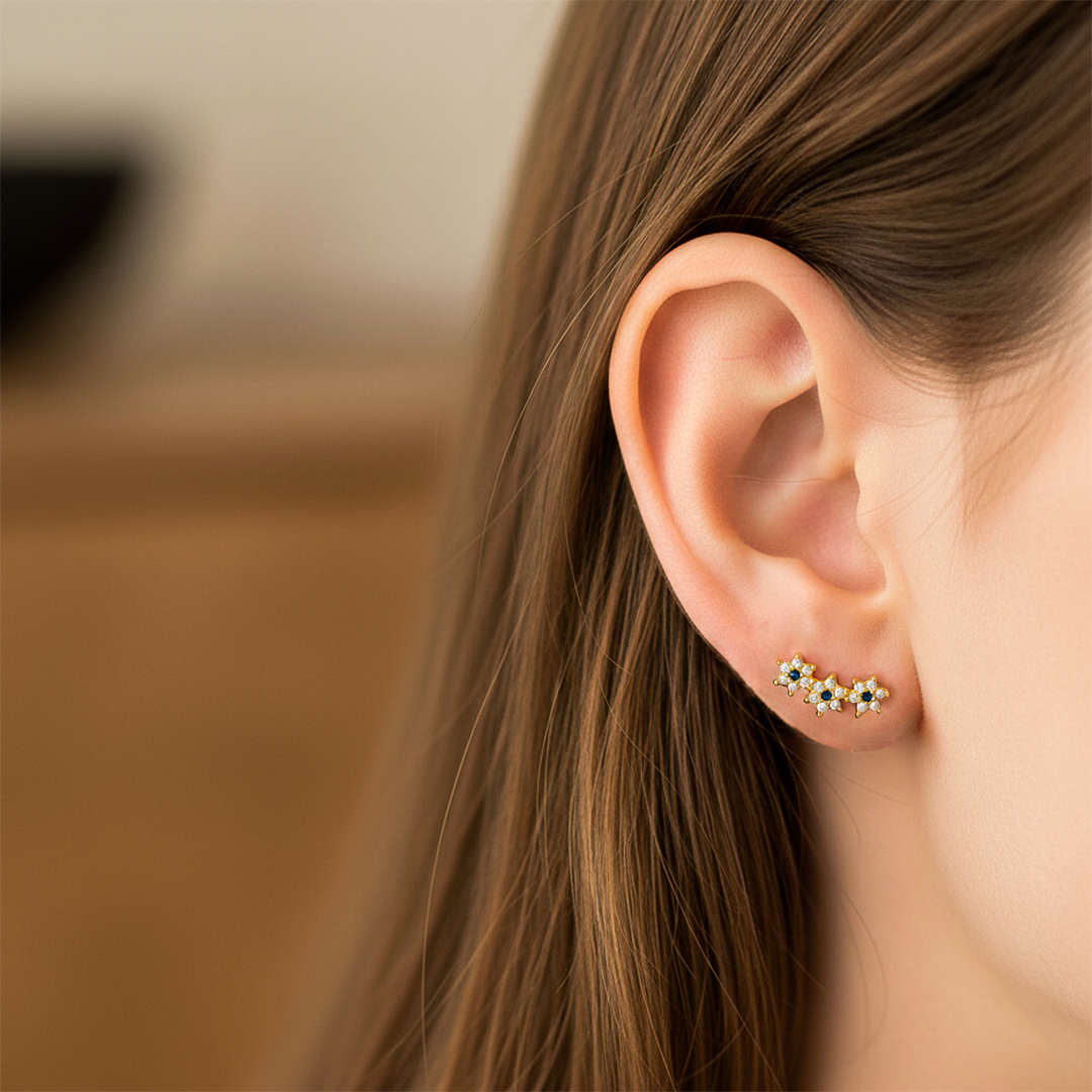 Oreja de modelo usando un topito en forma de caterpillar de 3 flores en oro amarillo de 18 quilates con cristales de color blanca y azul de Joyería Caracas. 