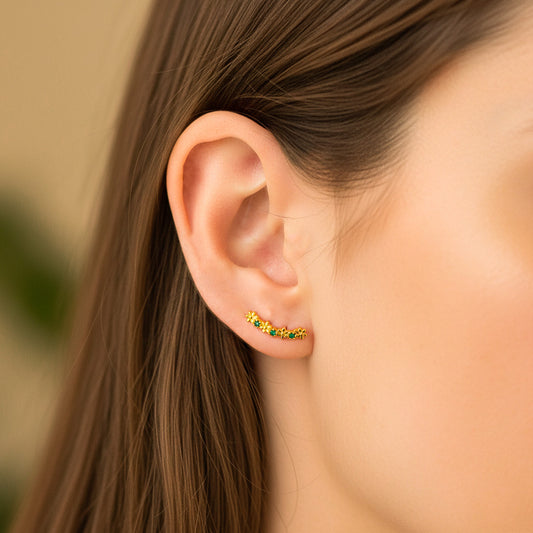 Oreja de modelo usando un topito caterpillar con formas de flores en oro amarillo de 18 quilates con cristales de color verde de Joyería Caracas. 