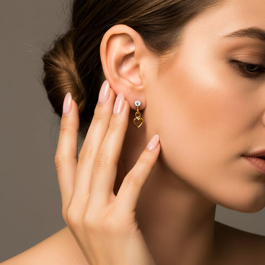 Oreja de modelo usando un topito colgante con la silueta de un corazón en oro amarillo de 18 quilates con cristal de color blanco de Joyería Caracas. 