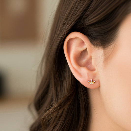 Oreja de modelo usando un topito en forma de corona en oro amarillo de 18 quilates con cristales de Joyería Caracas. 