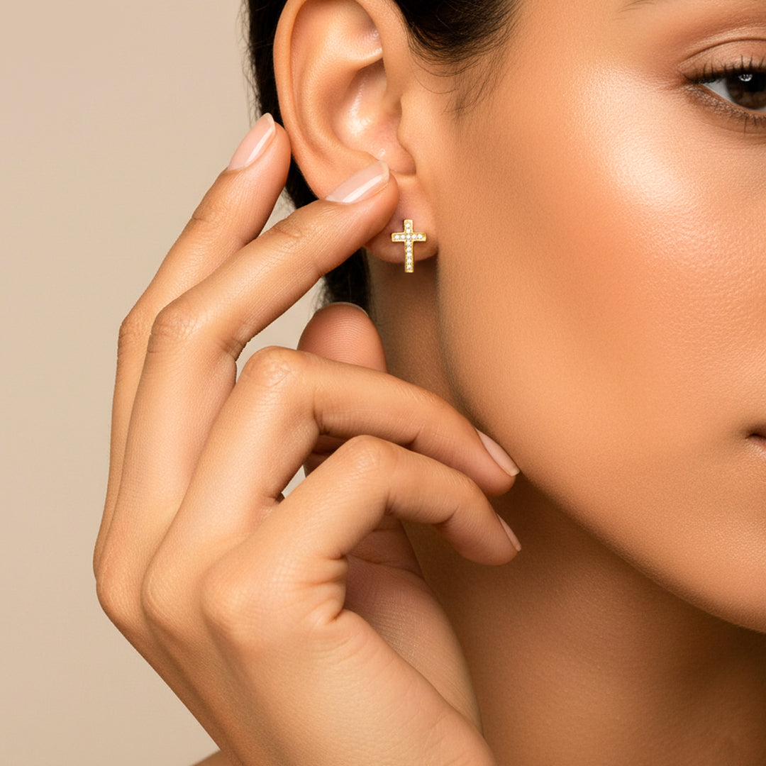 Oreja de modelo usando un topito en forma de cruz en oro amarillo de 18 quilates con cristales de color blanco de Joyería Caracas.
