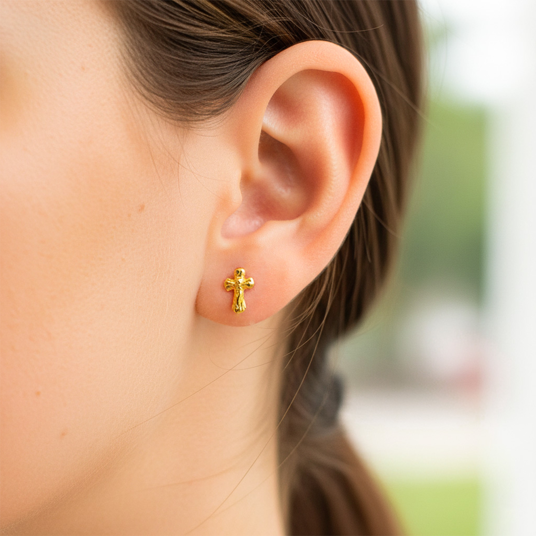 Oreja de modelo usando un topito en forma de cruz con cristo en oro amarillo de 18 quilates de Joyería Caracas. 