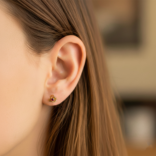 Oreja de modelo usando un topito en forma de espiral en oro amarillo de 18 quilates con cristal de color rojo de Joyería Caracas. 