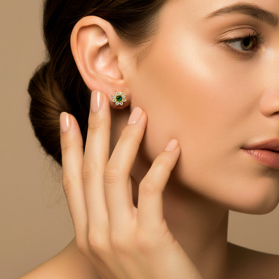 Oreja de modelo usando un topito en forma de flor en oro amarillo de 18 quilates con cristal de color verde y blancos alrededor de Joyería Caracas. 
