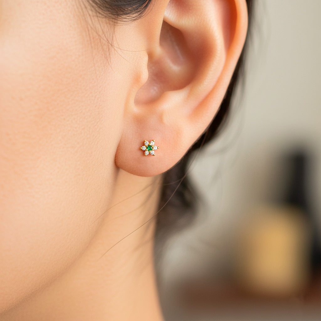 Oreja de modelo usando un topito en forma de flor en oro amarillo de 18 quilates con cristales de color blanco y verde de Joyería Caracas. 