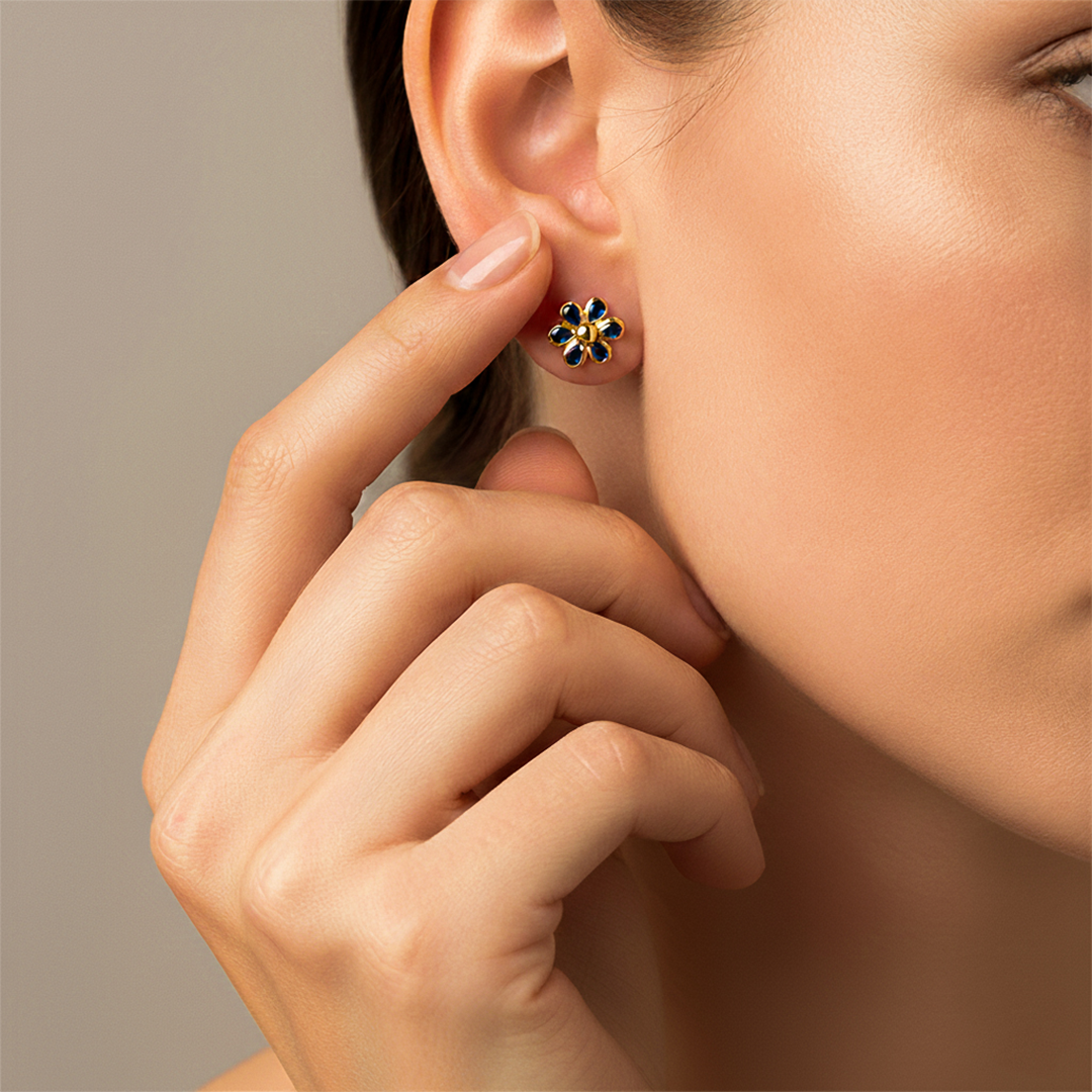 Oreja de modelo usando un topito en forma de flor en oro amarillo de 18 quilates con cristales de color azul oscuro de Joyería Caracas. 