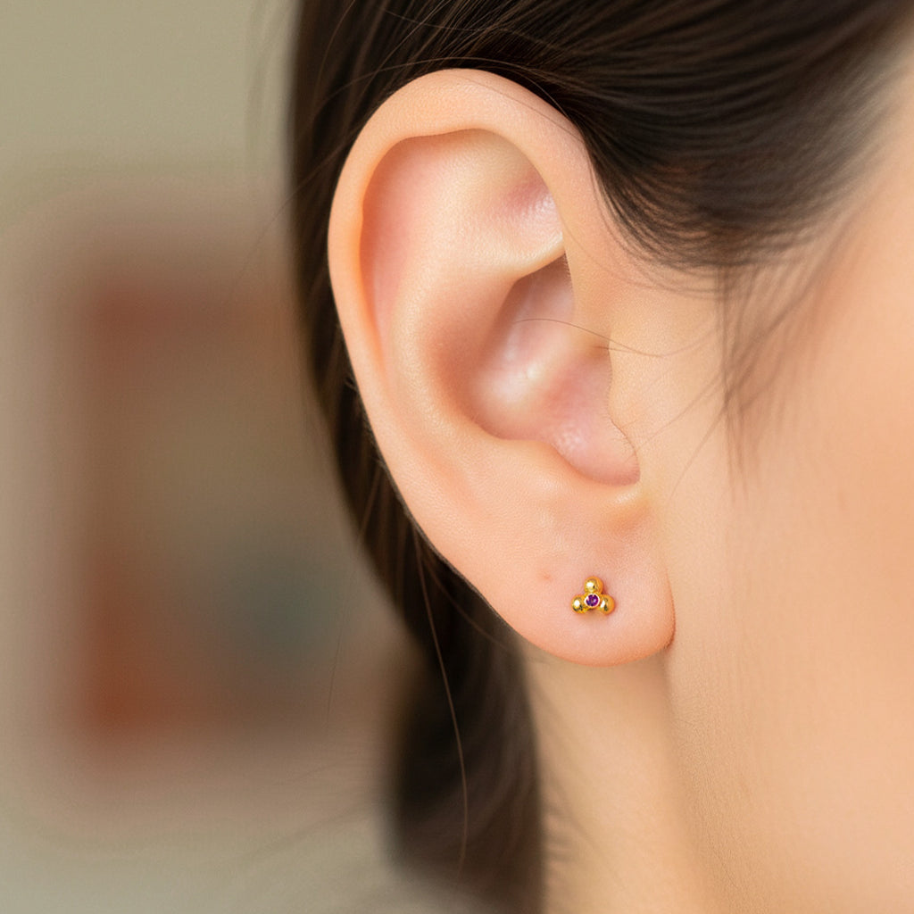 Oreja de modelo usando un topito en forma de flor de loto acanalada en oro amarillo de 18 quilates con cristal rojo en el centro de Joyería Caracas.