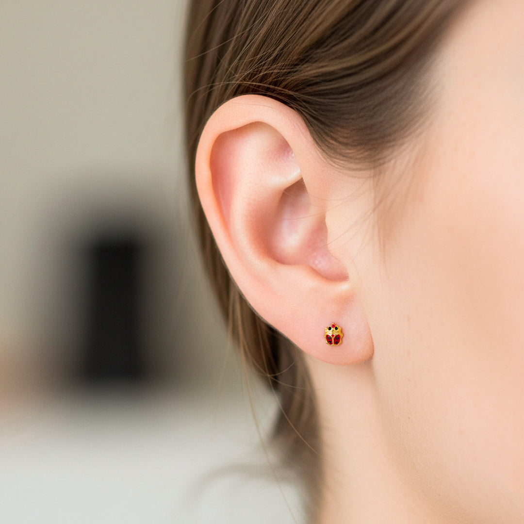 Oreja de modelo usando un topito en forma de lady bug en oro amarillo de 18 quilates de Joyería Caracas. 
