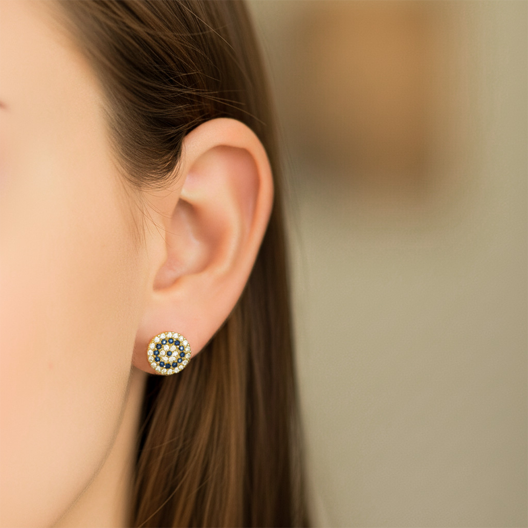 Oreja de modelo usando un topito en forma de rueda en oro amarillo de 18 quilates con cristales de color blanco y azul de Joyería Caracas. 