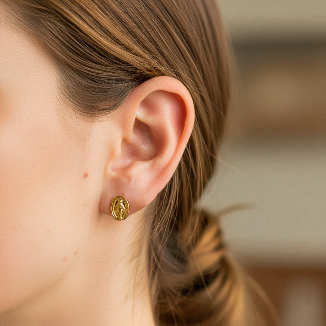 Oreja de modelo usando un topito de la Virgen de la Milagrosa en oro amarillo de 18 quilates de Joyería Caracas. 
