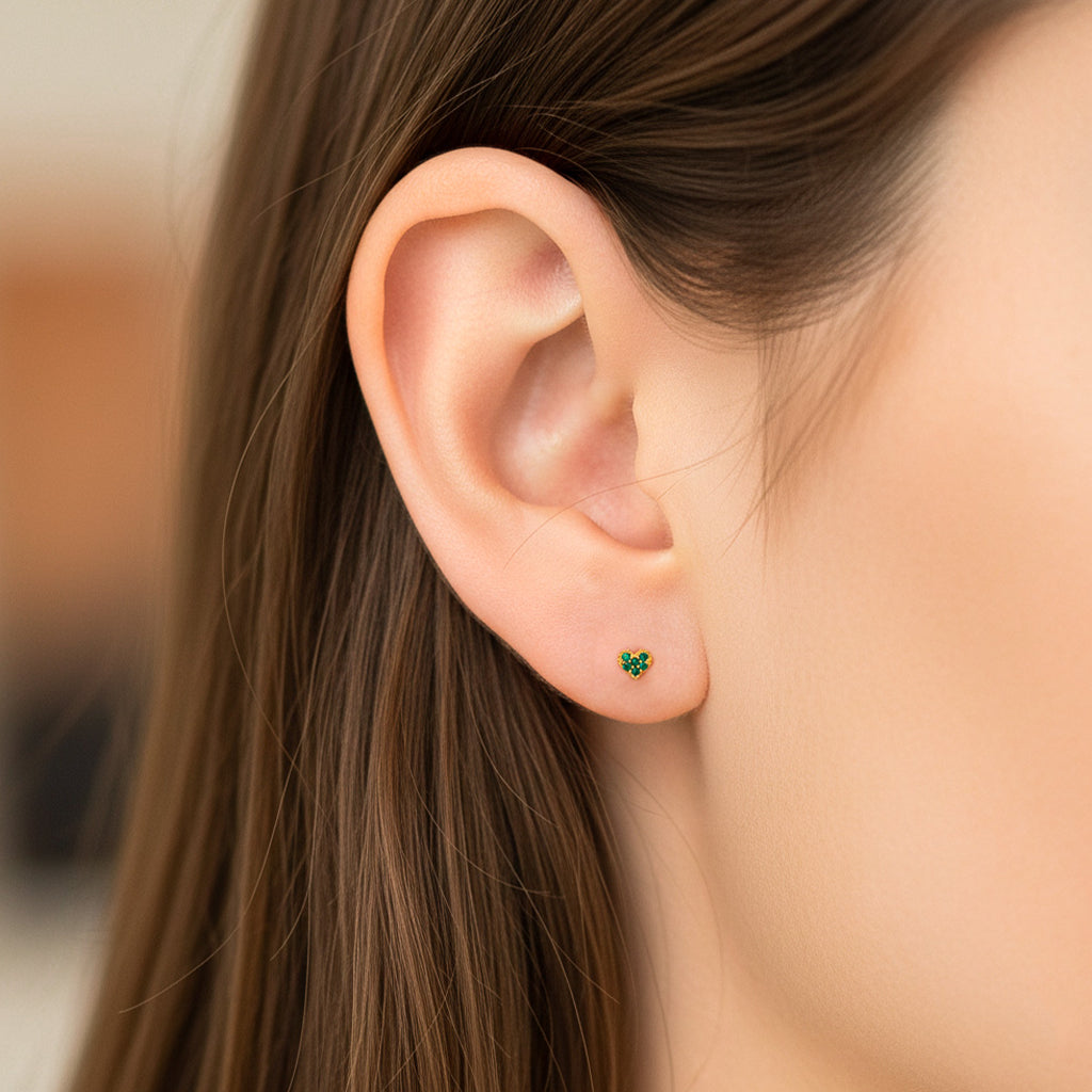 Oreja de modelo usando un topito en forma de corazón en oro amarillo de 18 quilates con cristales de color verde de Joyería Caracas. 