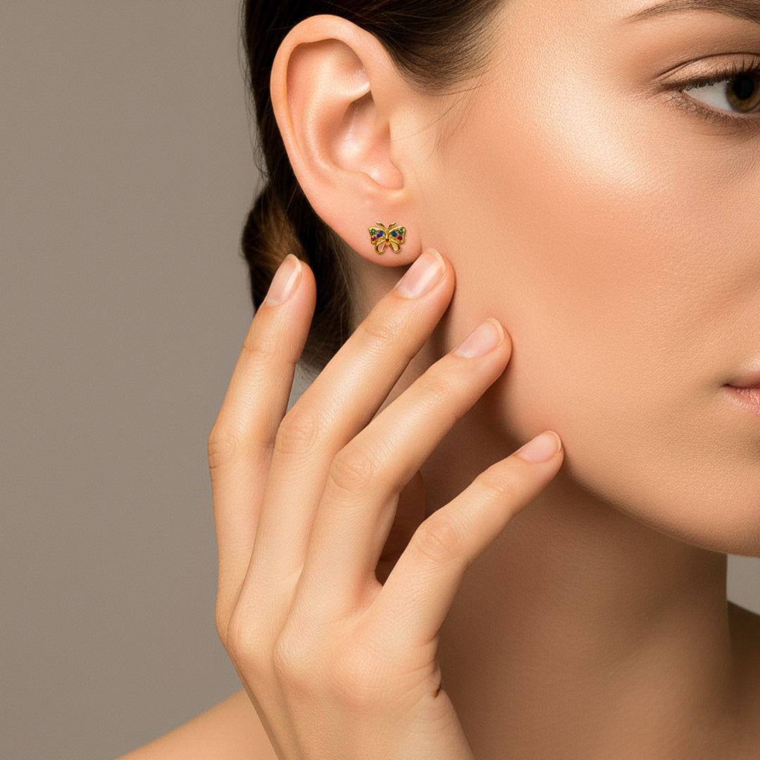 Oreja de modelo usando un topito en forma de mariposa en oro amarillo de 18 quilates con cristales de distintos colores de Joyería Caracas. 