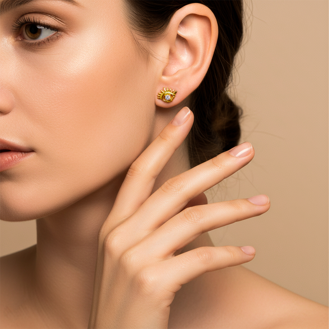 Oreja de modelo usando un topito en forma de ojo turco en oro amarillo de 18 quilates con cristal de color blanco de Joyería Caracas. 