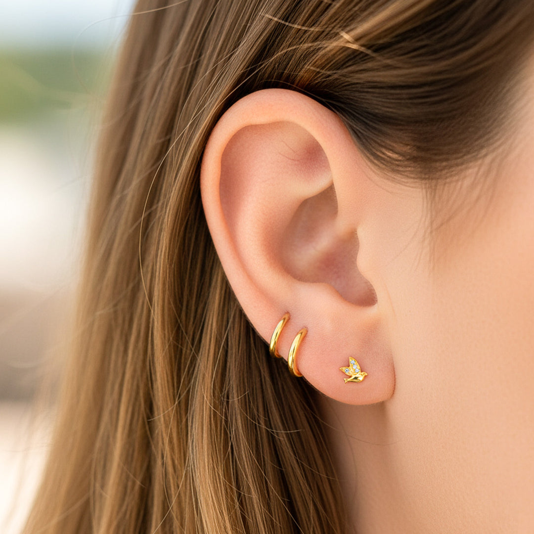 Oreja de modelo usando un topito en forma de paloma en oro amarillo de 18 quilates con cristales de Joyería Caracas. 
