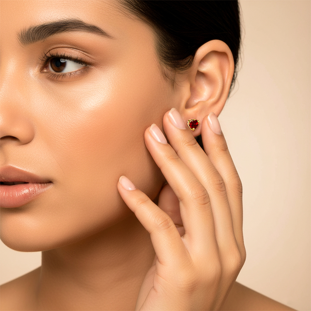 Oreja de modelo usando un topito en forma de corazón en oro amarillo de 18 quilates con cristal de color rojo en forma de corazón de Joyería Caracas. 