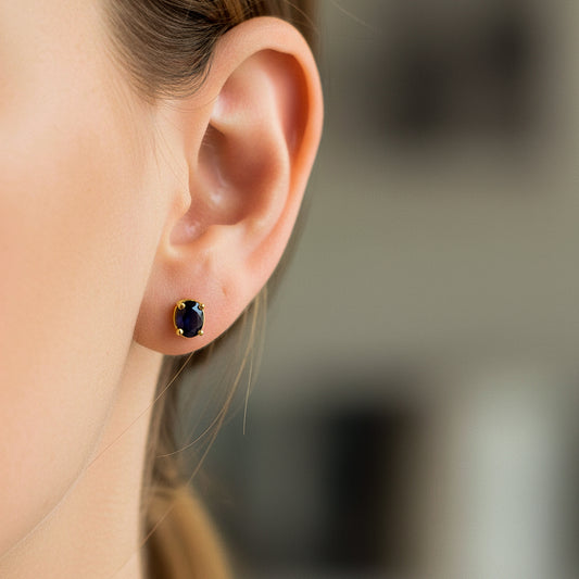 Oreja de modelo usando un topito ovalado en oro amarillo de 18 quilates con cristal de color azul de Joyería Caracas. 