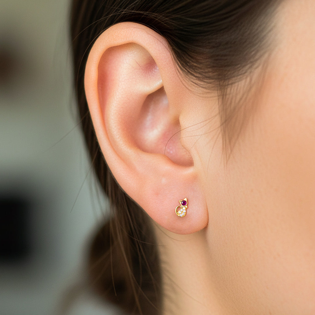 Oreja de modelo usando un topito en forma de gato en oro amarillo de 8 quilates con cristal de color rojo y blancos de Joyería Caracas. 
