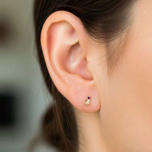 Oreja de modelo usando un topito en forma de gato en oro amarillo de 8 quilates con cristal de color rojo y blancos de Joyería Caracas. 