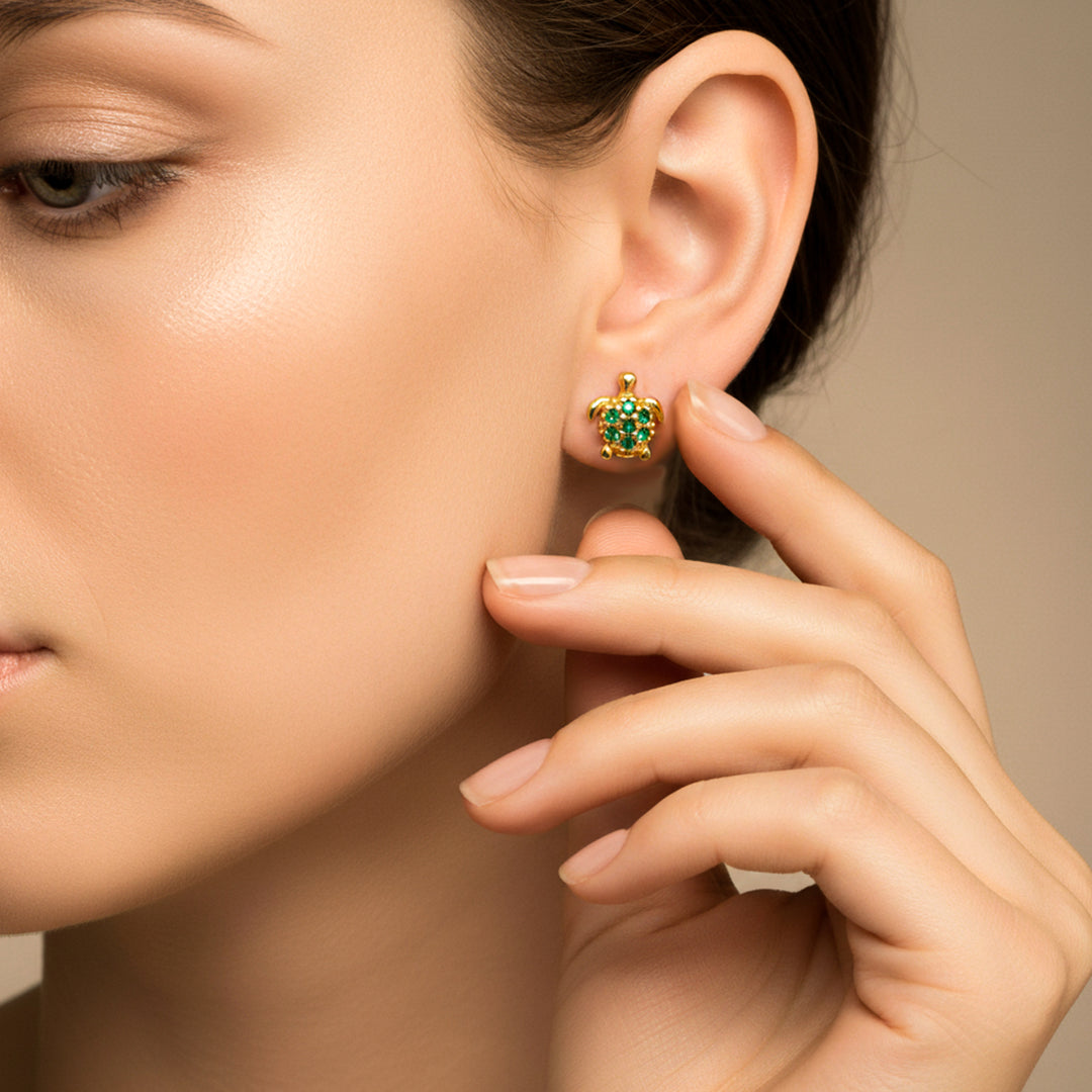 Oreja de modelo usando unos topitos en forma de tortuga en oro amarillo de 18 quilates con cristales de color verde de Joyería Caracas. 