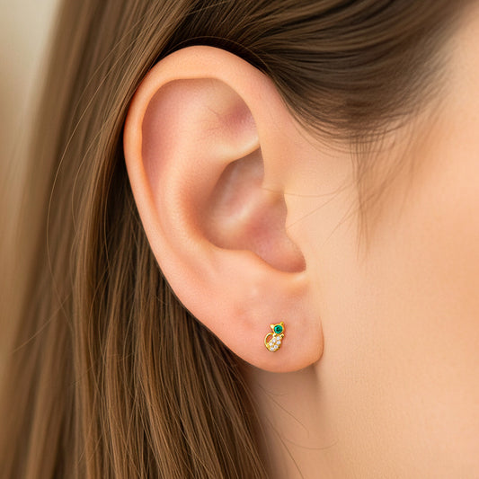 Oreja de modelo usando un topito en forma de gato en oro amarillo de 18 quilates con cristal de color verde y blancos de Joyería Caracas. 